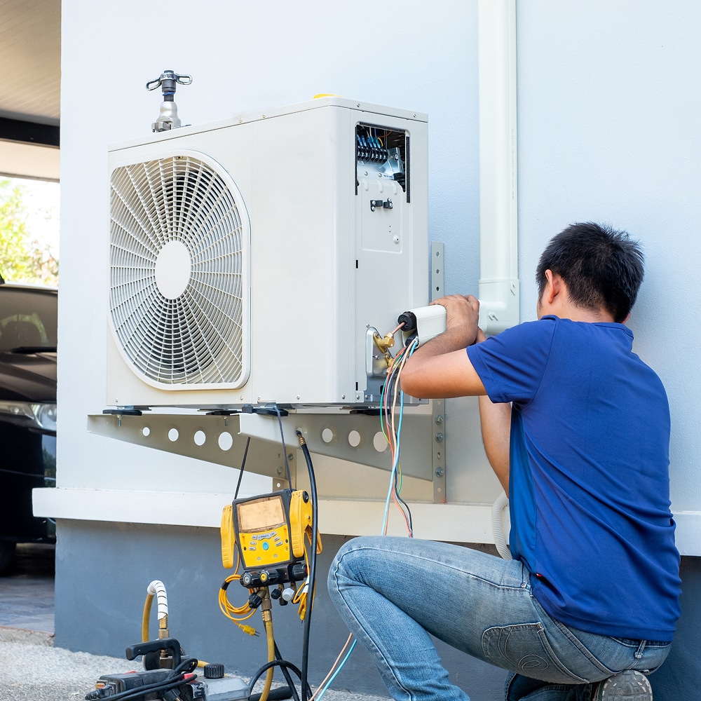 Technicien installant une unité extérieure de climatisation sur un support mural avec des outils de mesure.